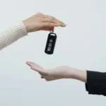 Two hands exchange a black car key fob with three buttons.