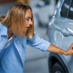 Driver examines car door scratch in parking garage, highlighting the need to fix small car dents quickly.