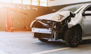 Car with front-end collision showing severe car frame damage inside an auto repair shop.