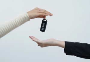 Two hands exchange a black car key fob with three buttons.